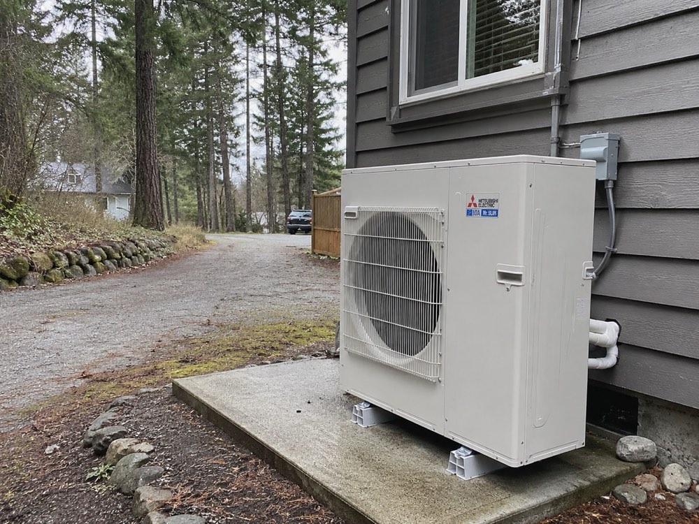 Outdoor heat pump unit on a concrete pad beside a house